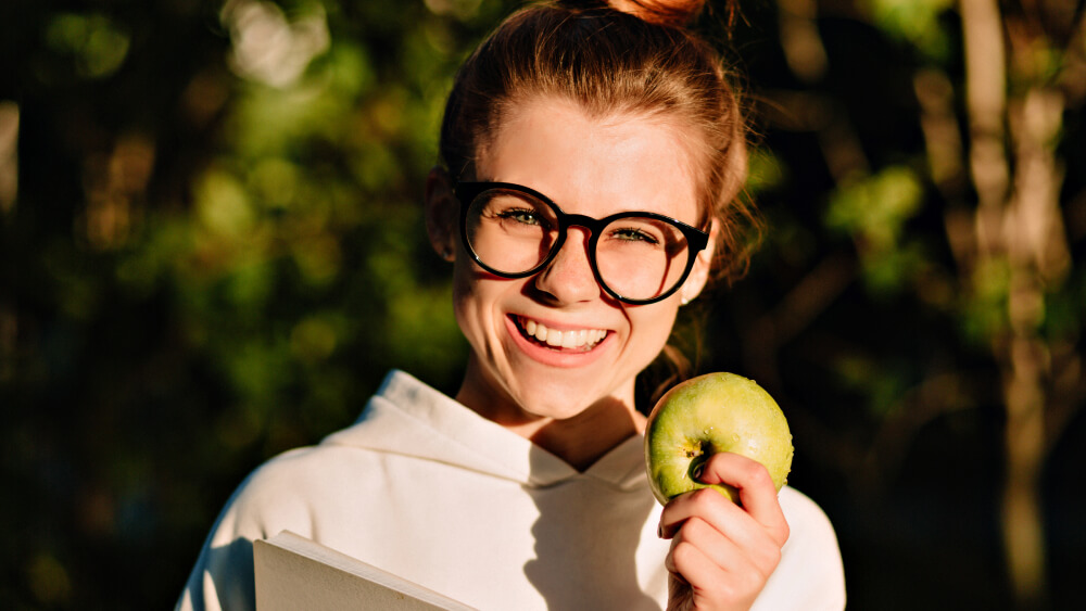 A kid eating green apple with glasses ready for school